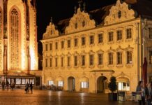 Filme und Medien ausleihen in Unterfranken: Wo Schulen und Gemeinden heute Material bekommen Das barocke Falkenhaus am Würzburger Marktplatz am Abend, links die beleuchtete Marienkapelle